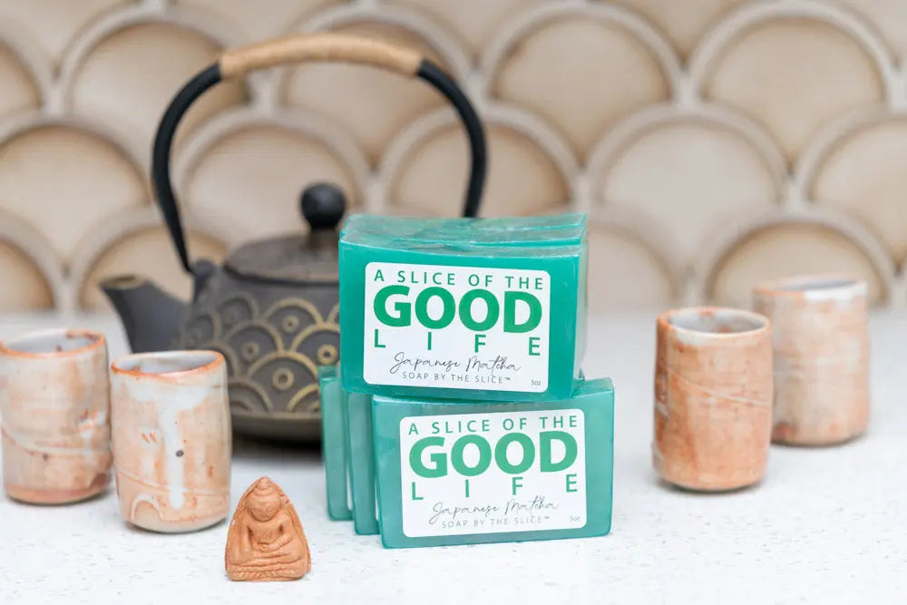 Stack of Japanese Matcha soap bars with a teapot, tea cups, and Buddha figurine.