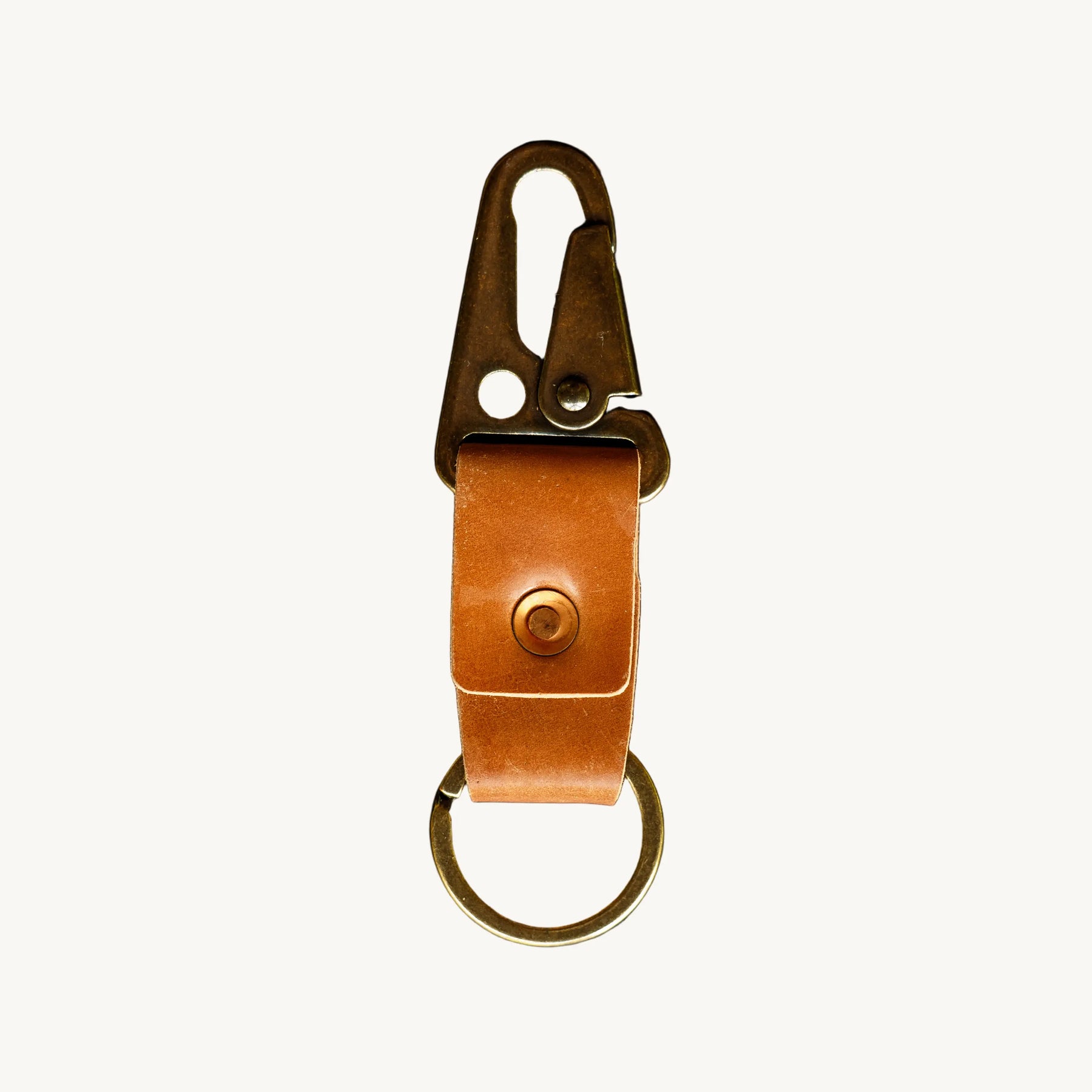 A key clip with brown leather strap, a brass lever clip, and an antique brass key ring on a white background.