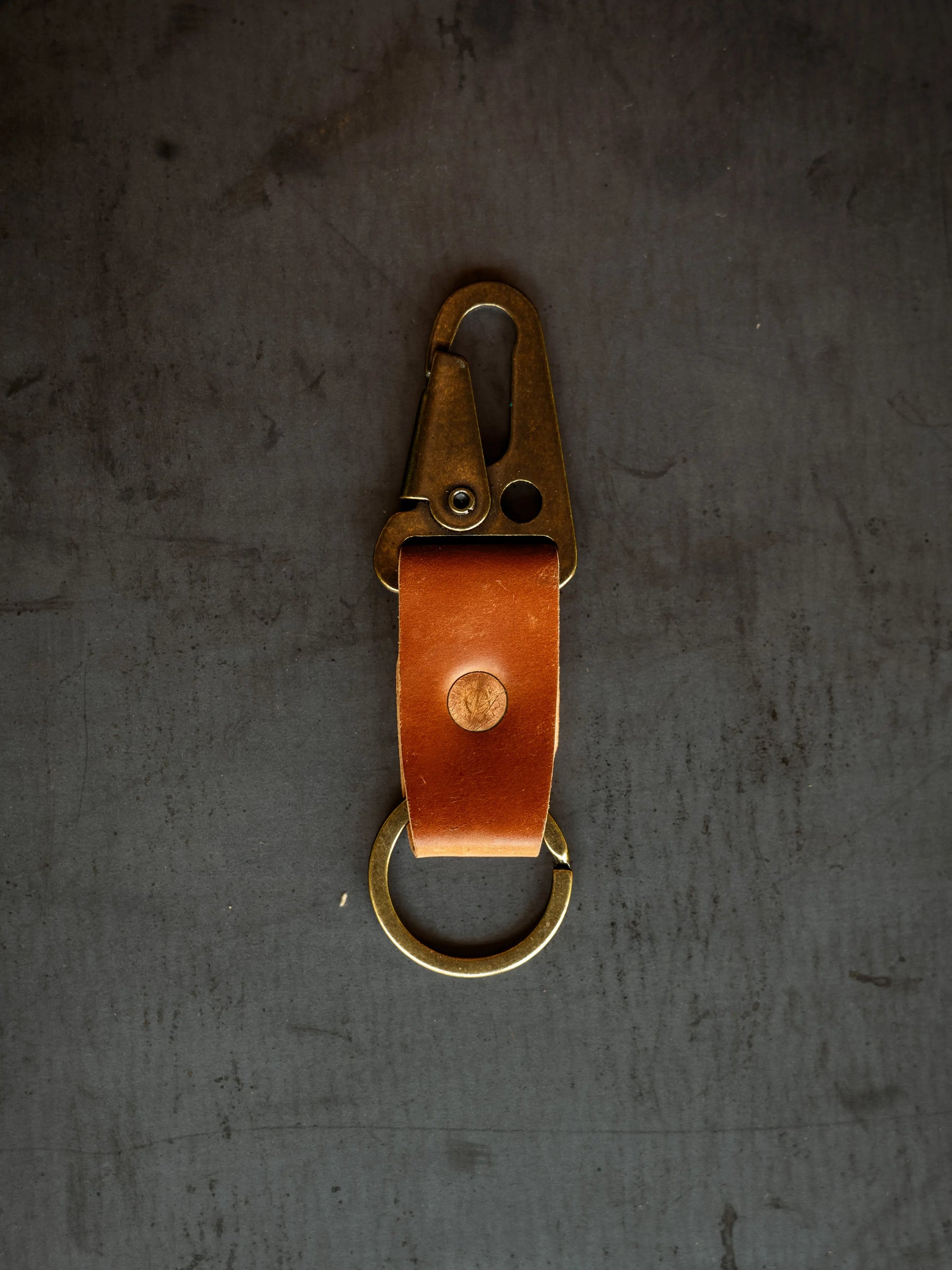 Brown leather key clip with brass clasp and keyring on a dark gray surface, close-up shot of Horween Shell Cordovan keychain.