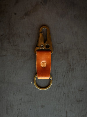 Brown leather key clip with brass clasp and keyring on a dark gray surface, close-up shot of Horween Shell Cordovan keychain.