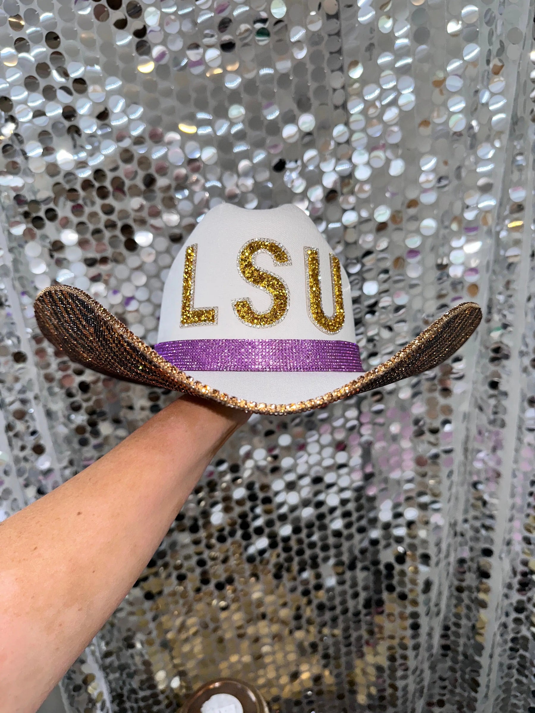 White cowgirl hat with gold LSU rhinestone letters and purple band.