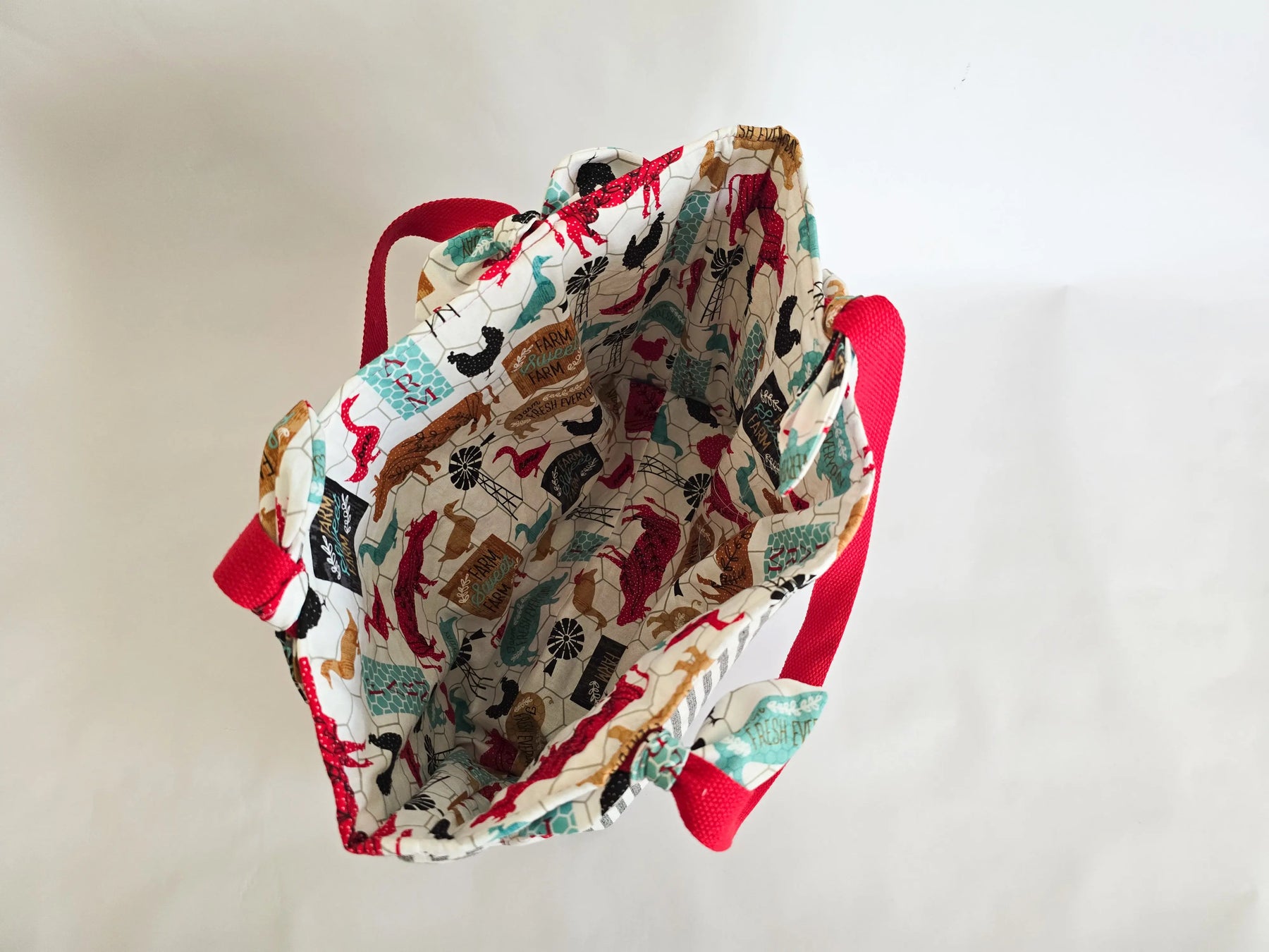 Handmade canvas tote bag with red straps, featuring farmhouse-themed animal and farm sign print interior fabric.
