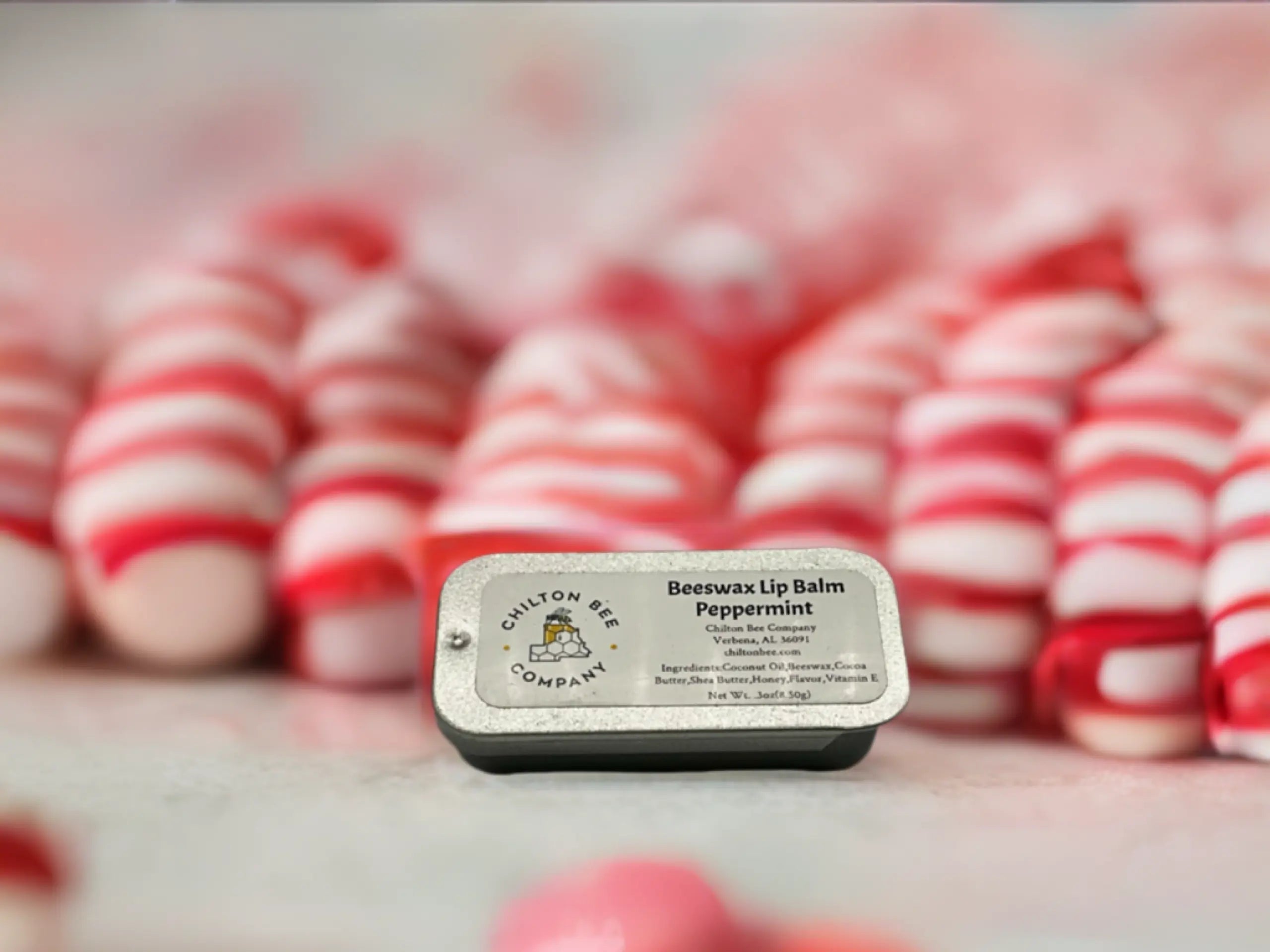 Chilton Bee Company Peppermint Beeswax Lip Balm tin surrounded by blurred red and white objects.