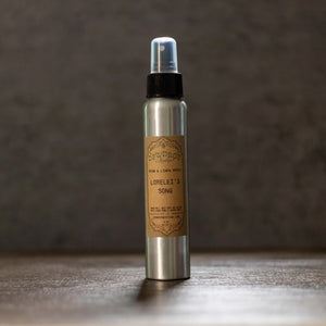 Dewdrop Mystique Lorelei's Song room and linen spray in a silver bottle with a brown label on a wooden surface.