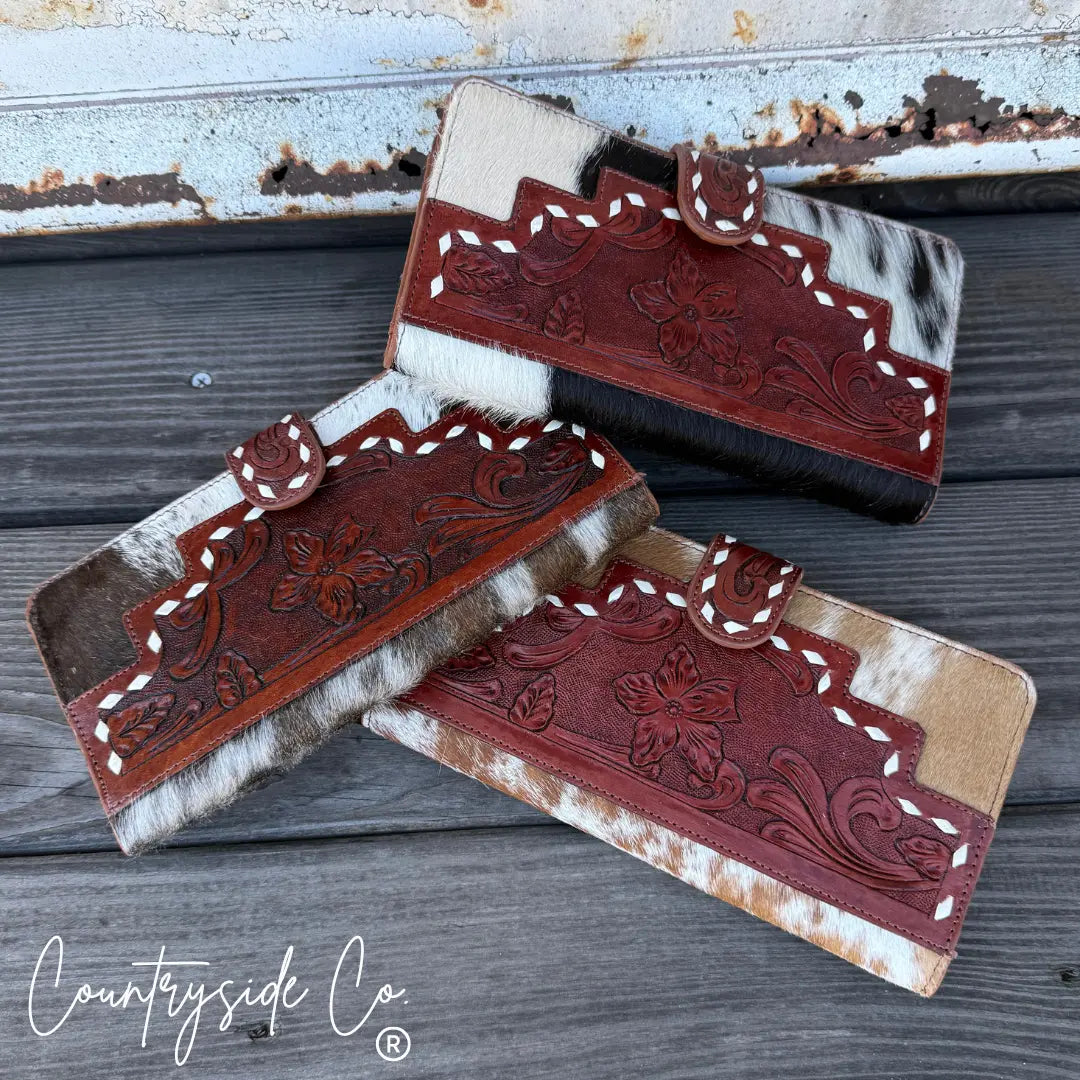 Three Loretta cowhide wallets with tooled leather details on a wooden surface.