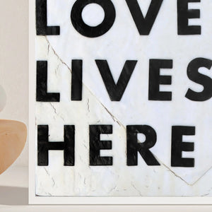 Love Lives Here art print with black textured letters on a cracked white background.
