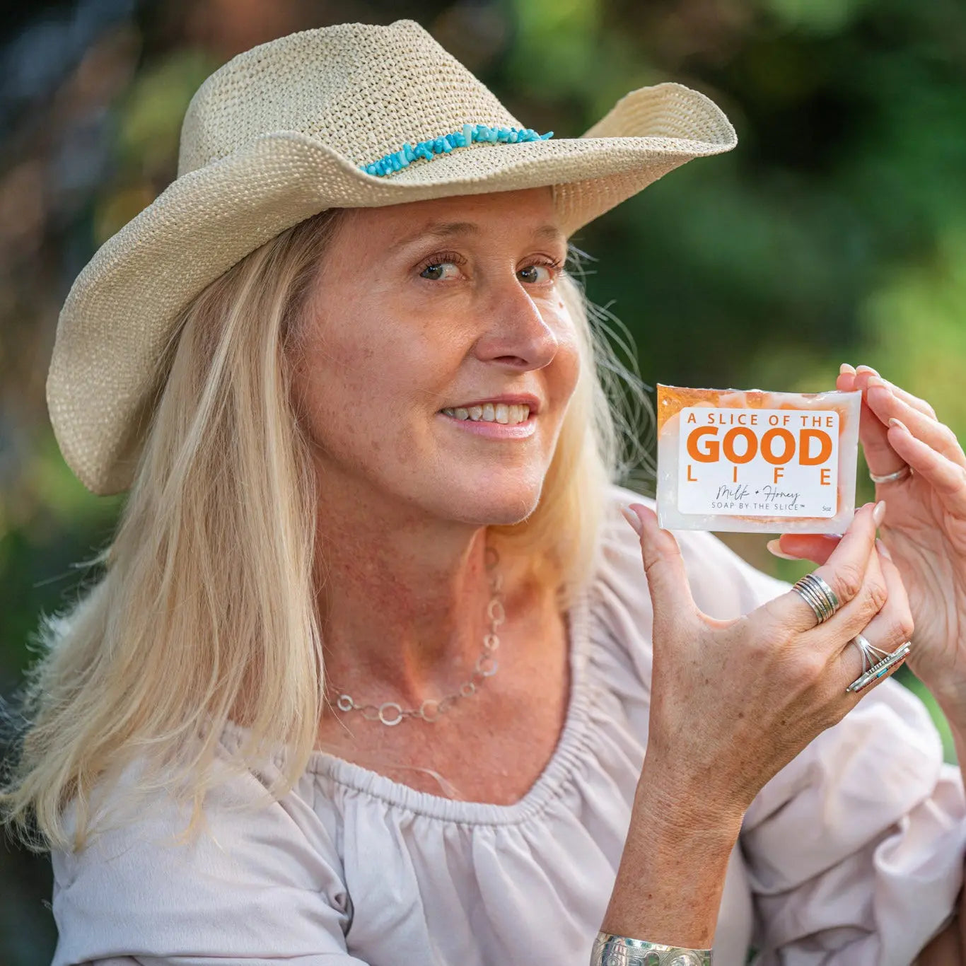 Woman in straw hat holding a slice of milk and honey soap with orange accents.