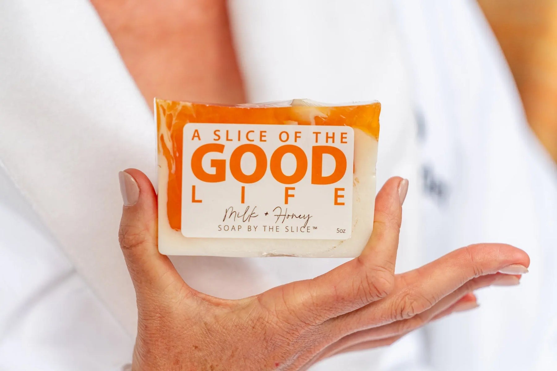 Hand holding a 5 oz Milk and Honey bar soap slice with orange and white swirls.