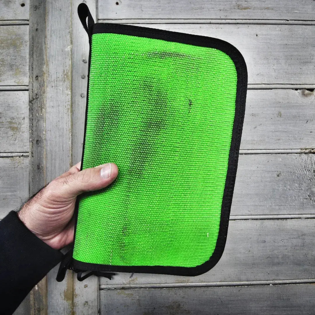 Bright green dopp bag with black trim held in a hand against a wooden background.