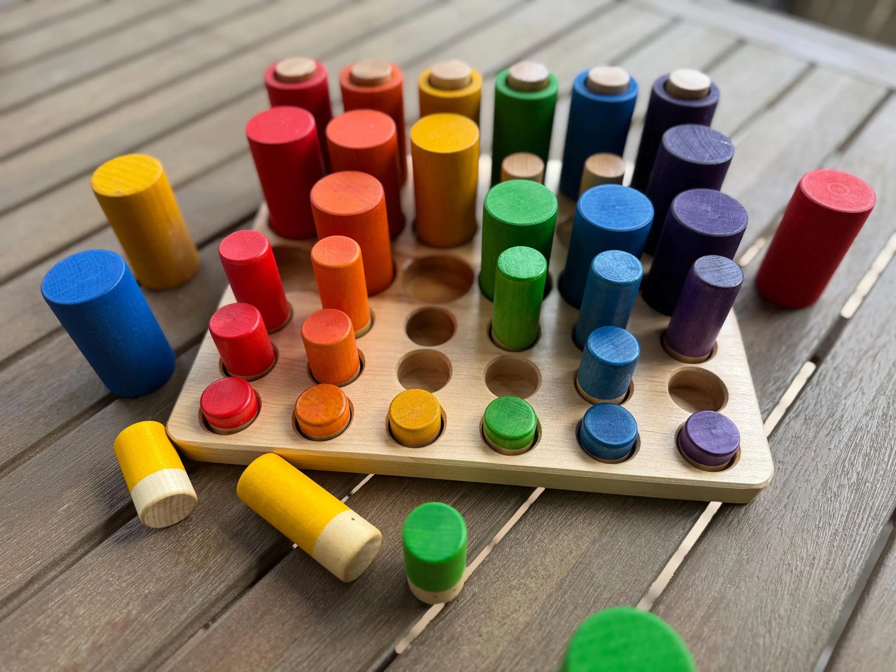 Wooden sorting tray with colorful pegs in red, orange, yellow, green, blue, and purple.