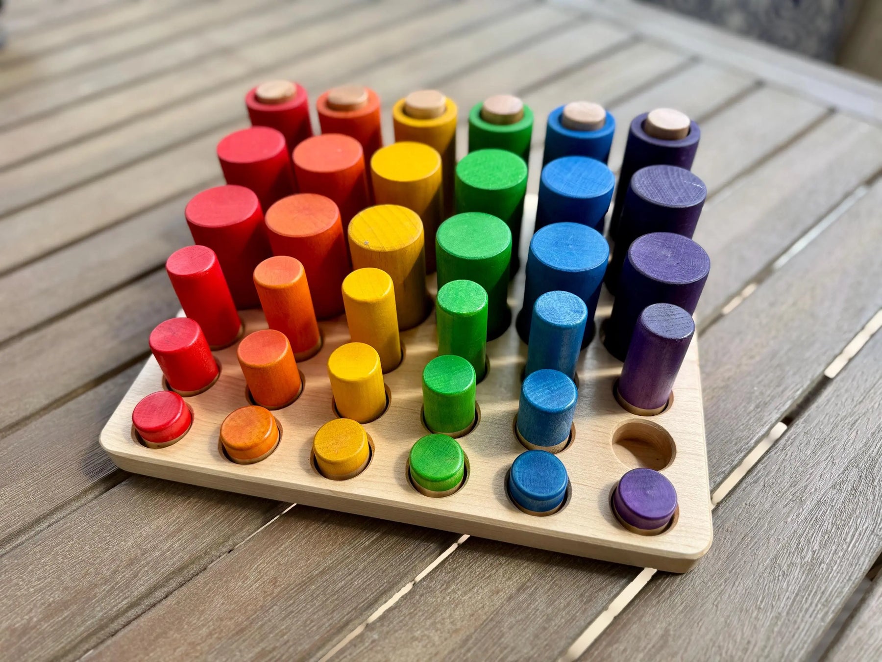 Wooden sorting tray with colorful cylinder pieces on a wooden table.