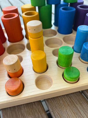 Wooden sorting tray with colorful cylindrical pieces in red, orange, yellow, green, and blue.