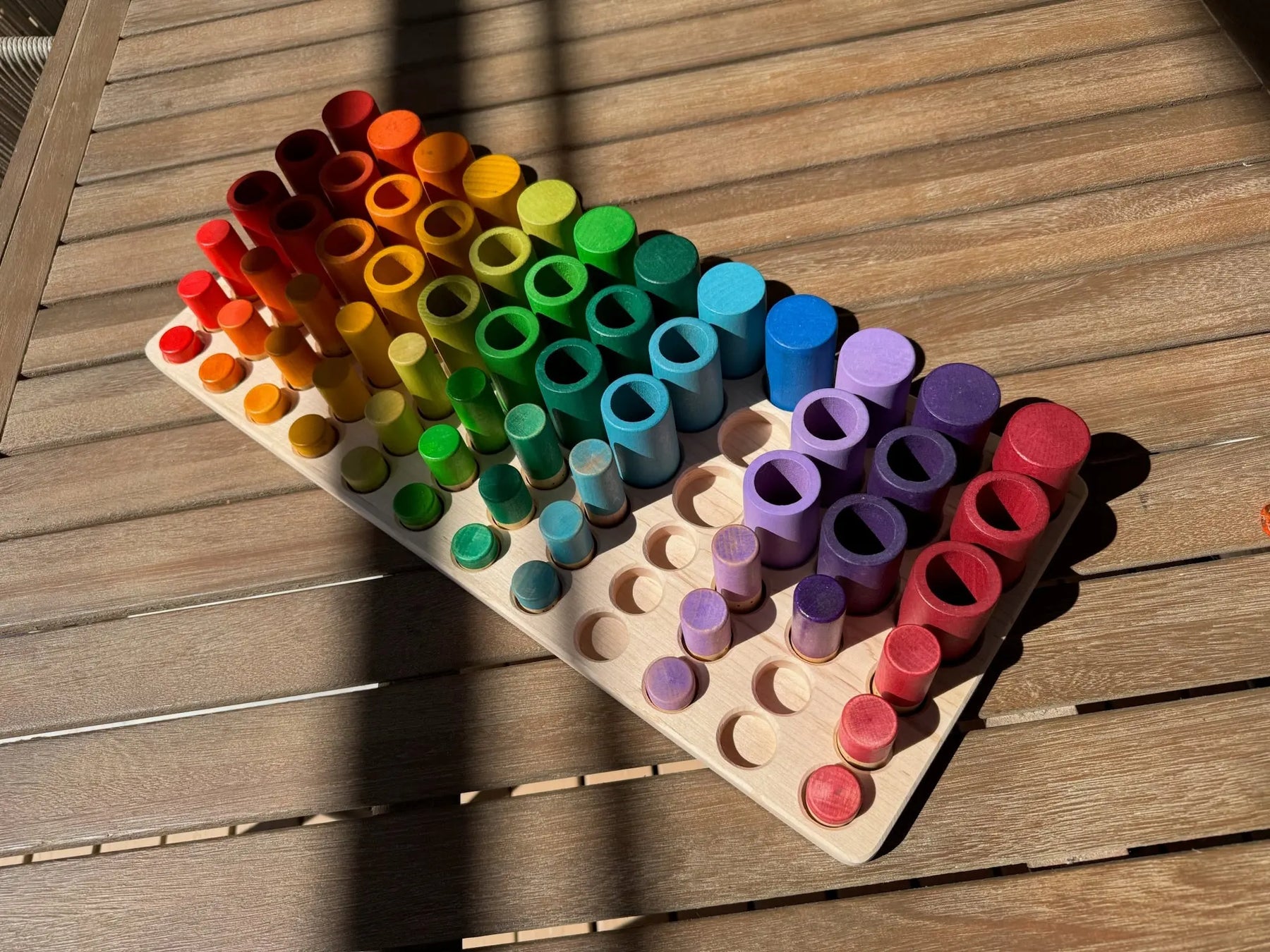 Wooden sorting tray with rows of colorful wooden cylinders arranged by color.