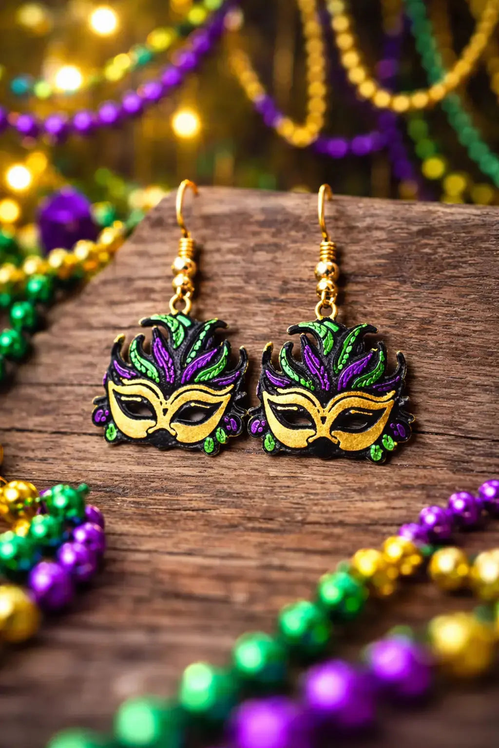 Mardi Gras mask earrings: purple, green, and gold masks on a wooden surface with matching beads.