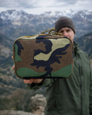 Man holding a woodland camouflage fanny pack with a zippered top.