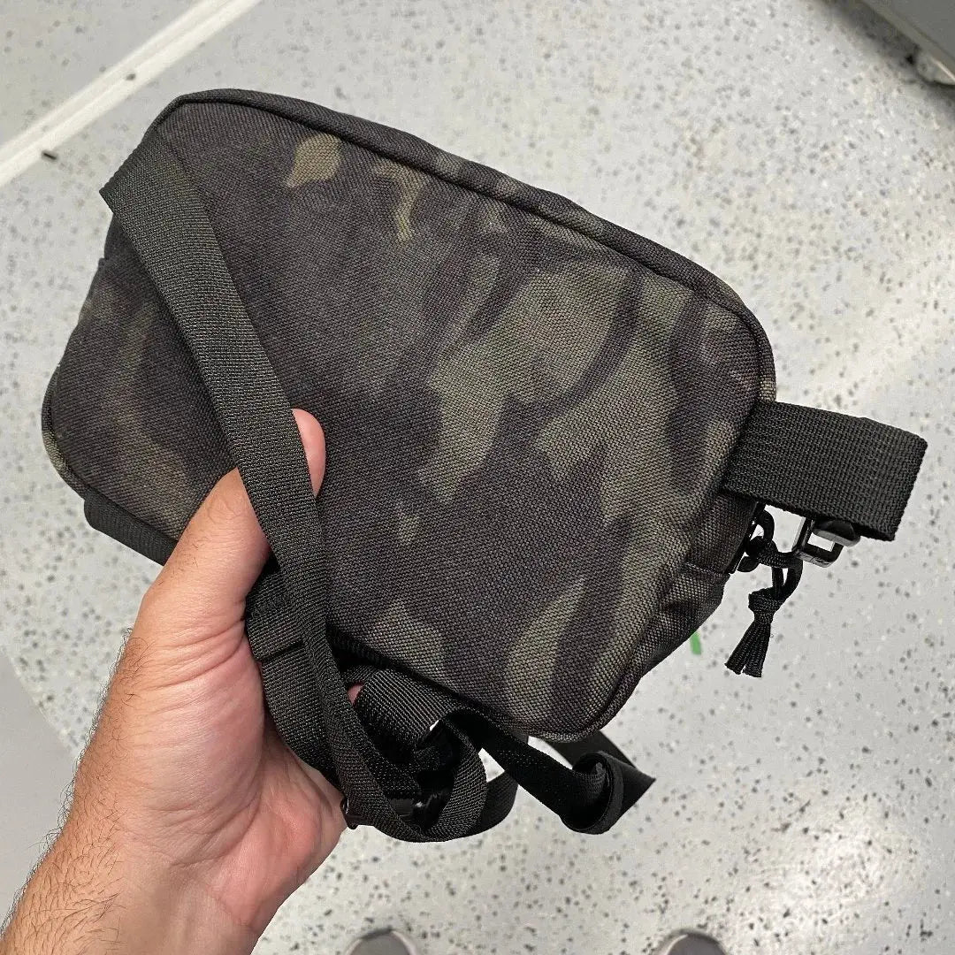 Hand holding a woodland camo fanny pack made of nylon with adjustable strap
