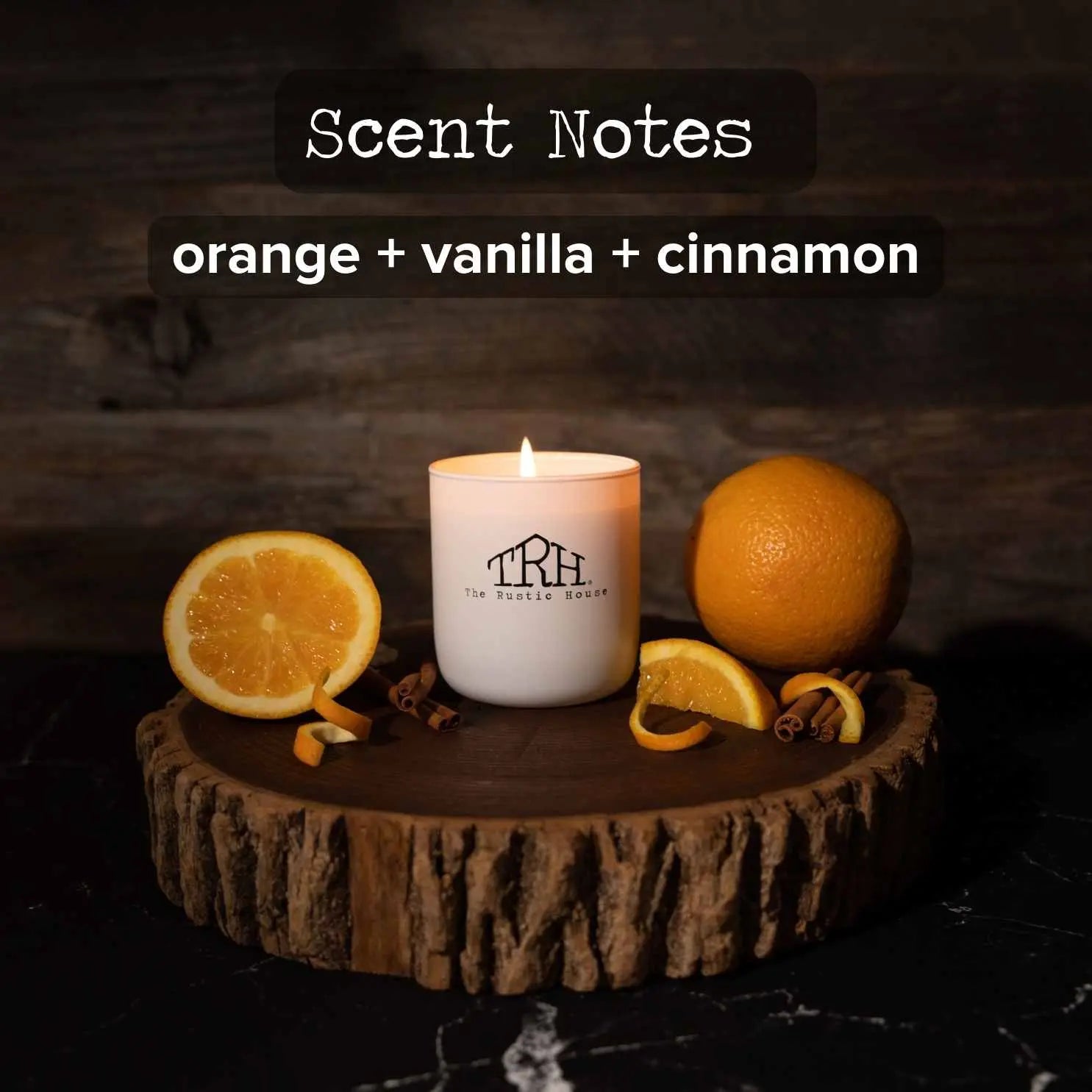 White scented candle with orange slices, whole orange, and cinnamon sticks on a wooden base.