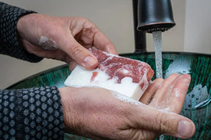 Hands washing with peppermint goat milk soap slice under running water