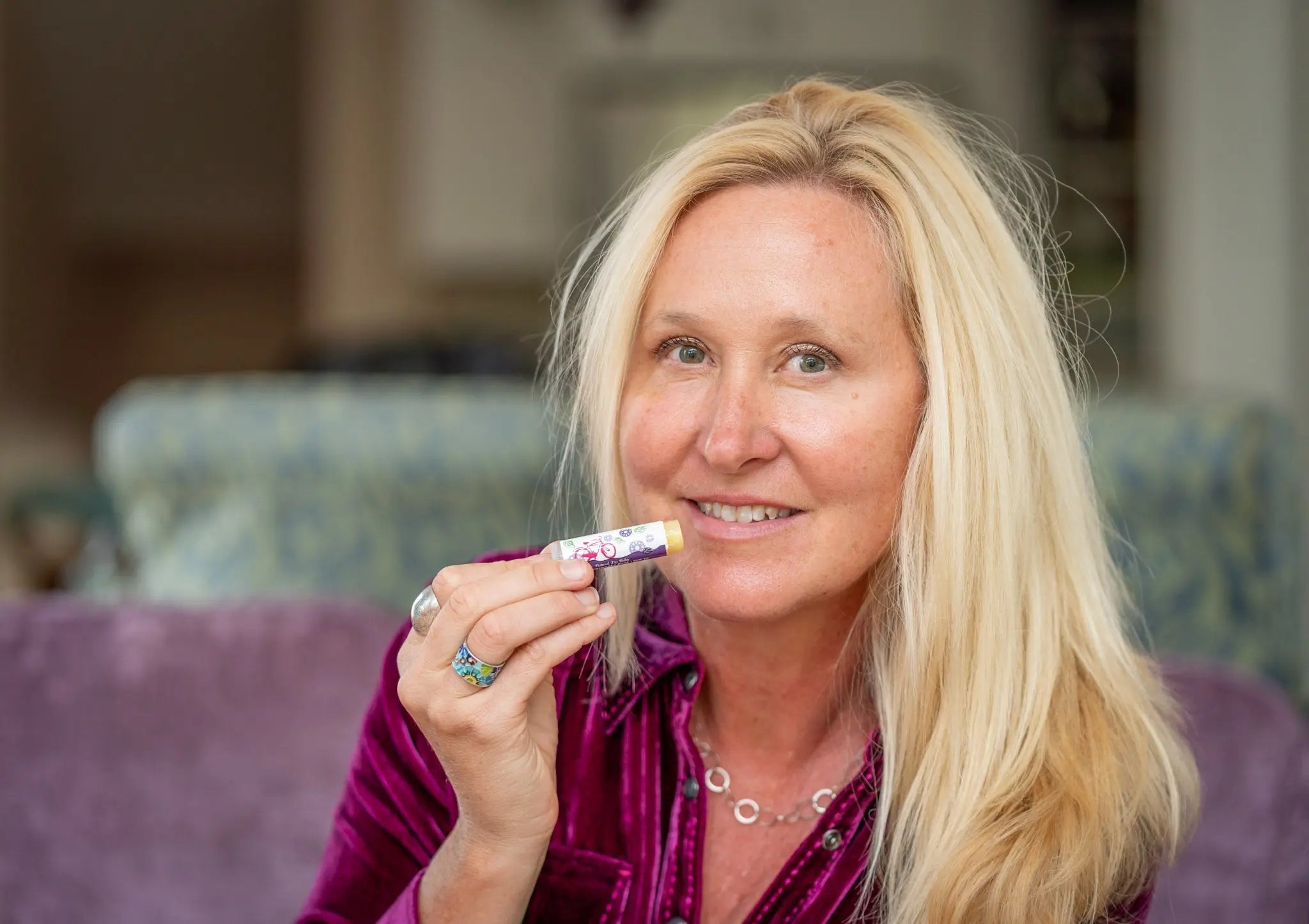 Woman holding a pomegranate acai lip balm tube with SPF 15 and a bike graphic.