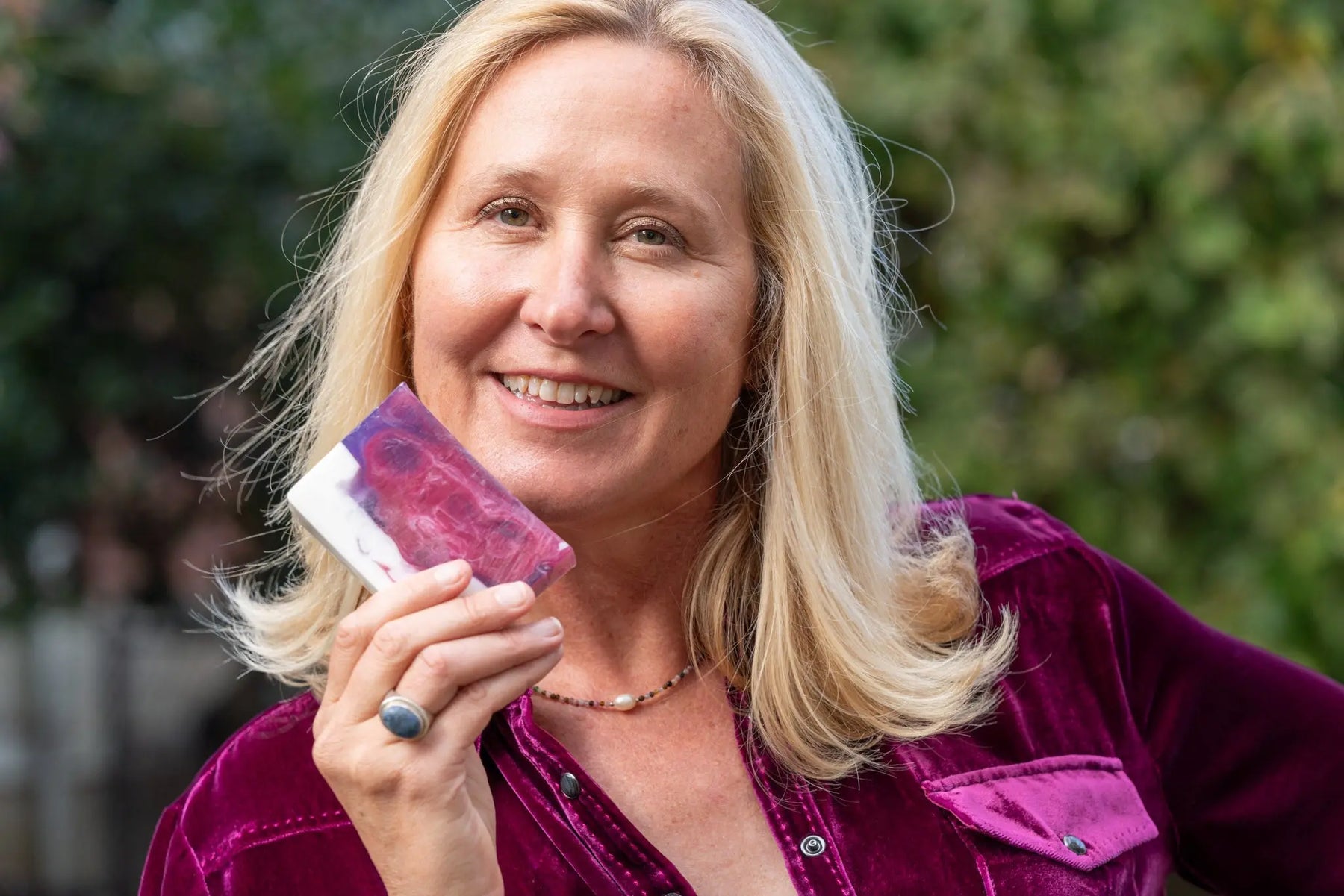 Woman holding a rectangular bar of POMEGRANATE GOAT'S MILK SOAP SLICE with purple and white swirls.