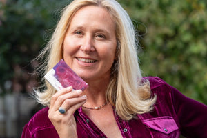 Woman holding a rectangular bar of POMEGRANATE GOAT'S MILK SOAP SLICE with purple and white swirls.
