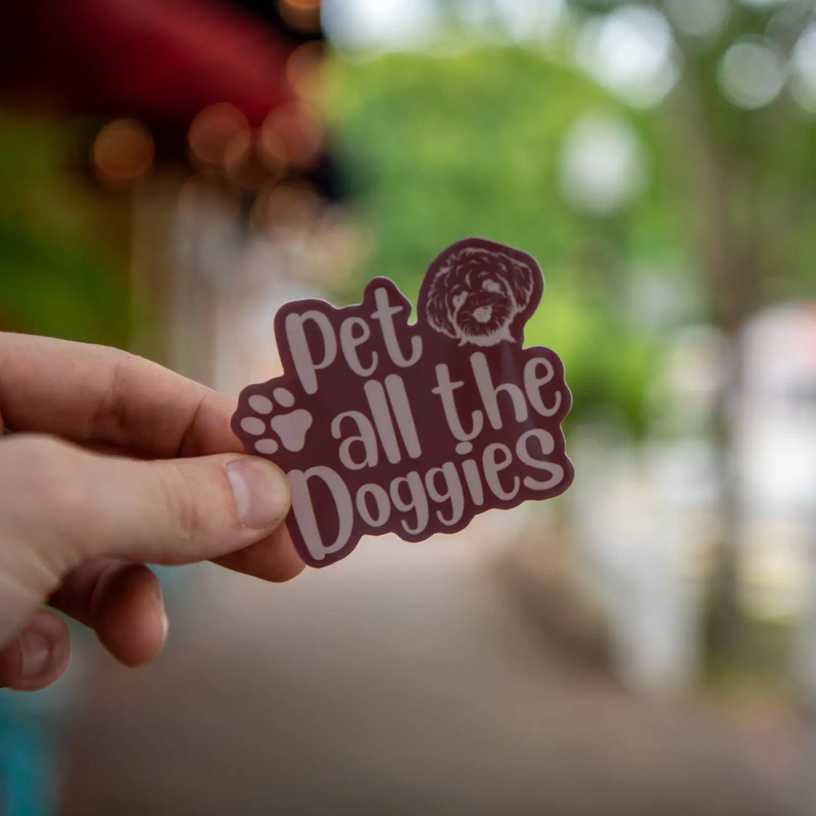A hand holds a "Pet all the Doggies" sticker with a dog illustration and paw print.