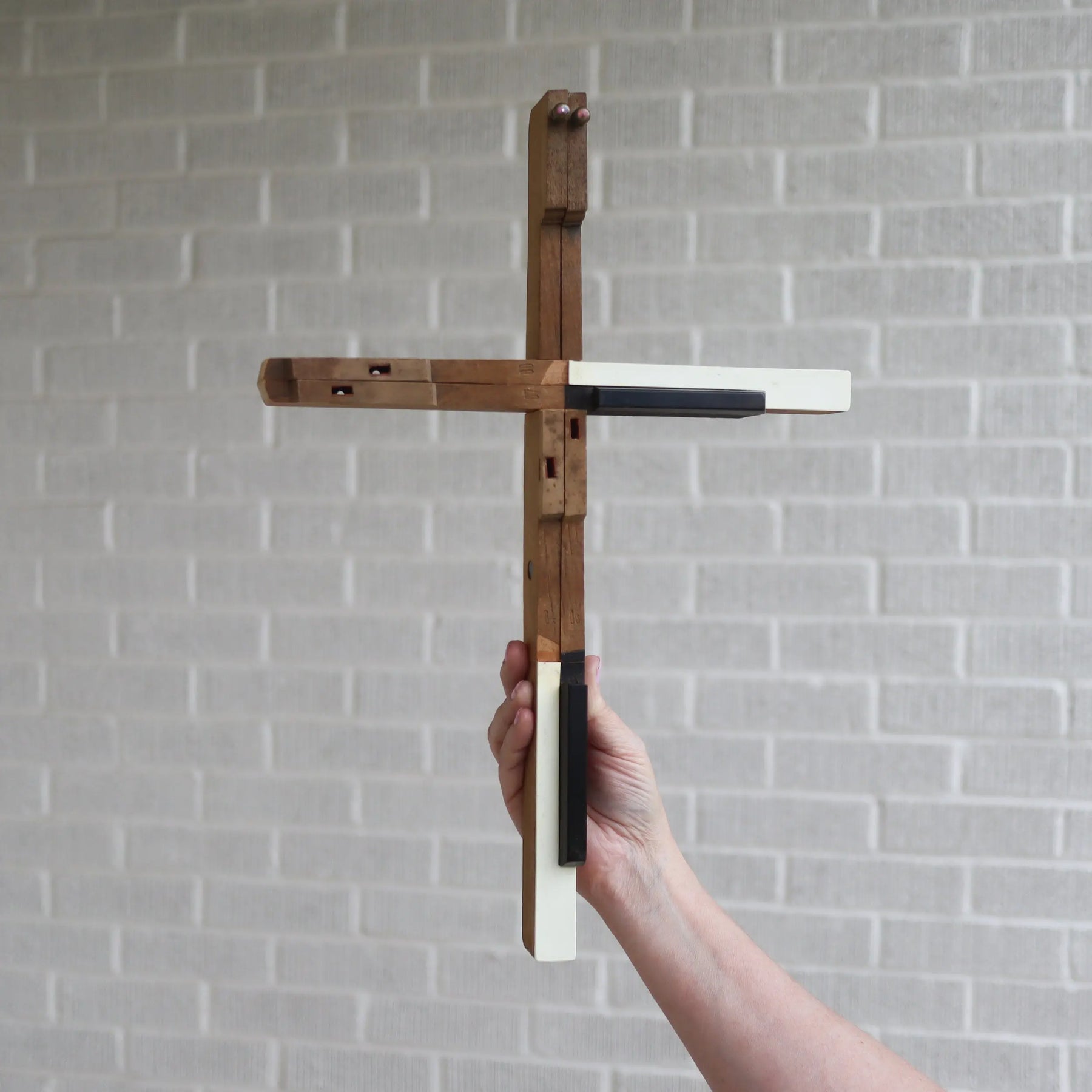 Handmade wooden cross with ivory and black piano key accents, held by a person.