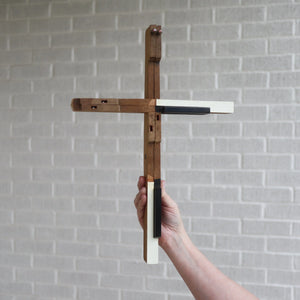Handmade wooden cross with ivory and black piano key accents, held by a person.