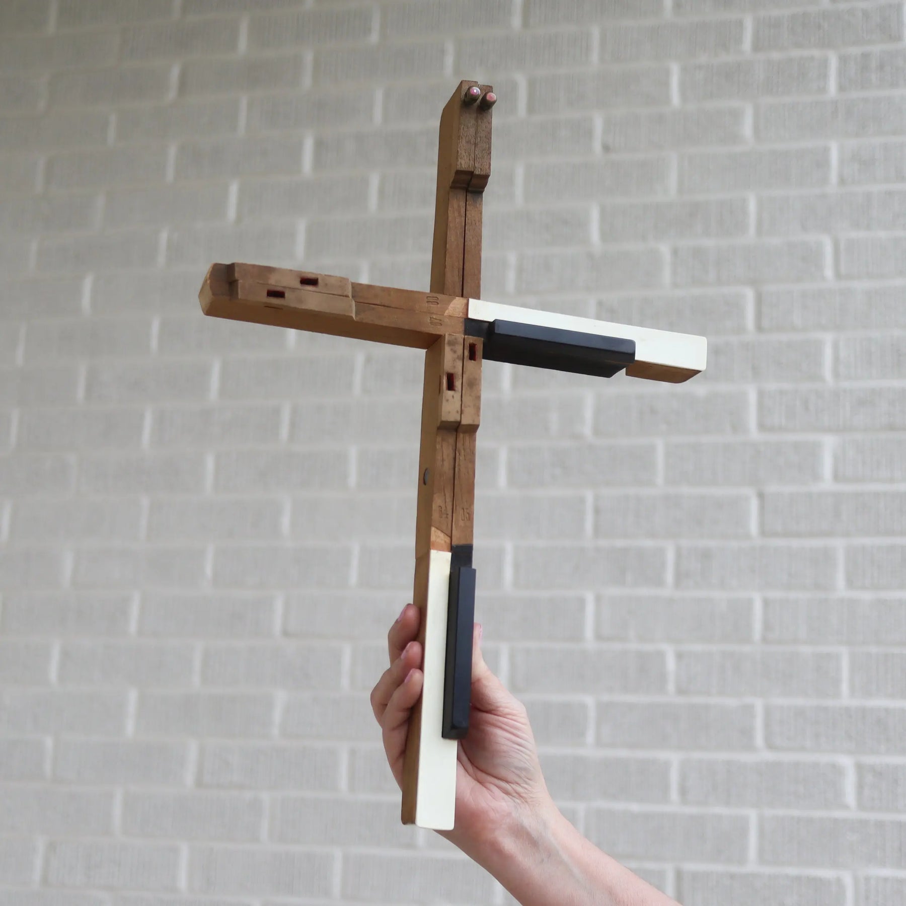 Wooden piano key cross with white and black accents held by a hand.