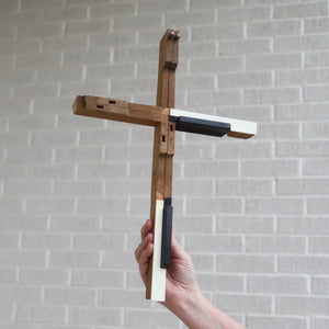 Wooden piano key cross with white and black accents held by a hand.