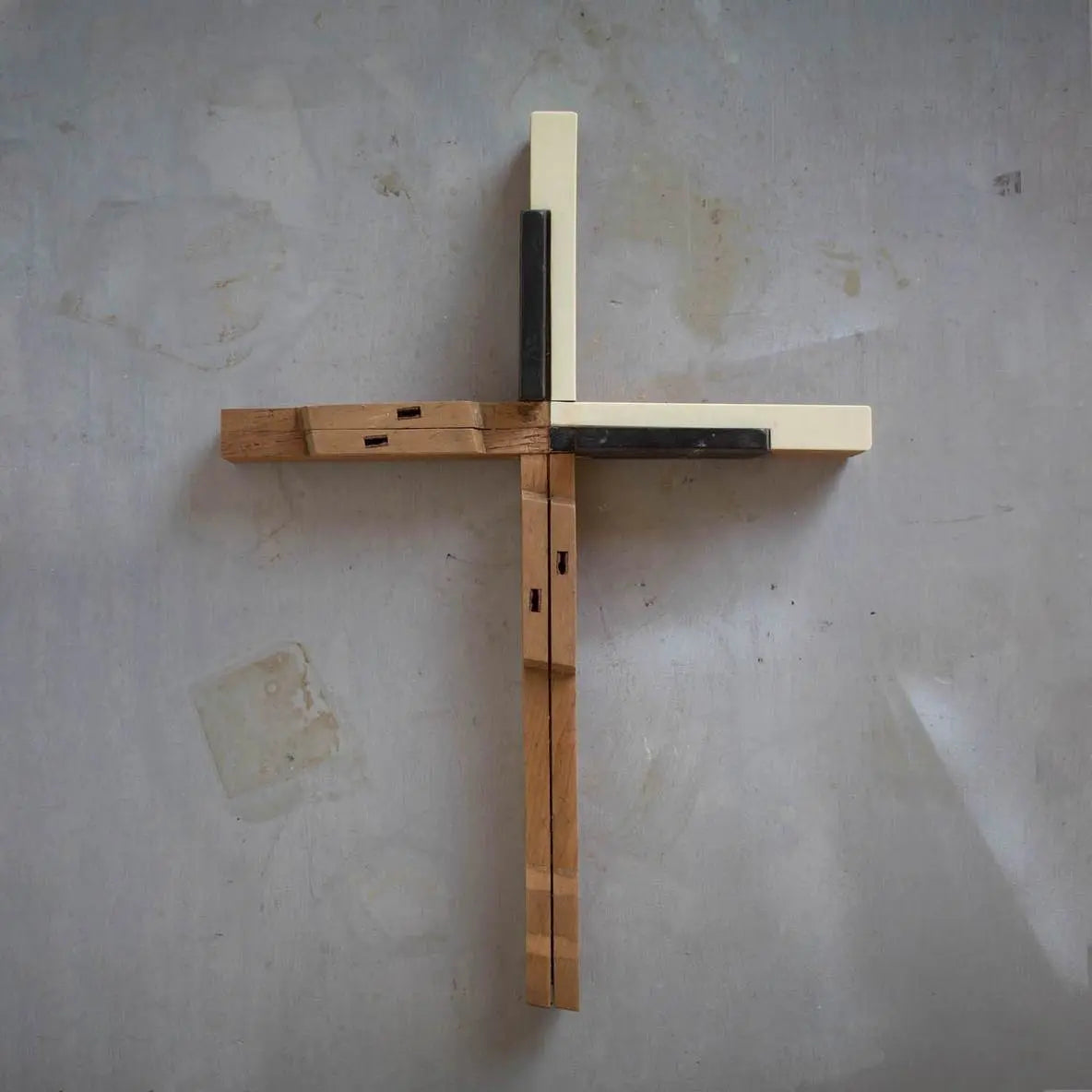 Wooden cross with bone-colored and dark accent pieces mounted on a textured wall.