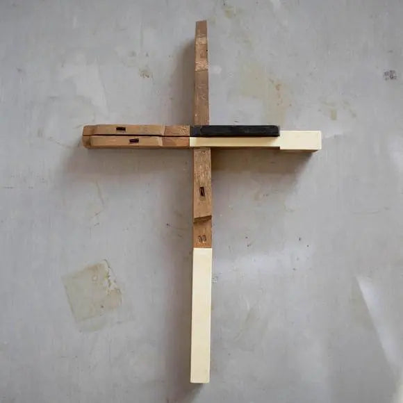 Cross made from reclaimed antique piano keys on a gray wall.