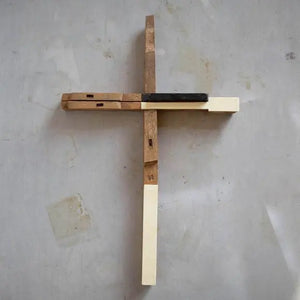 Cross made from reclaimed antique piano keys on a gray wall.