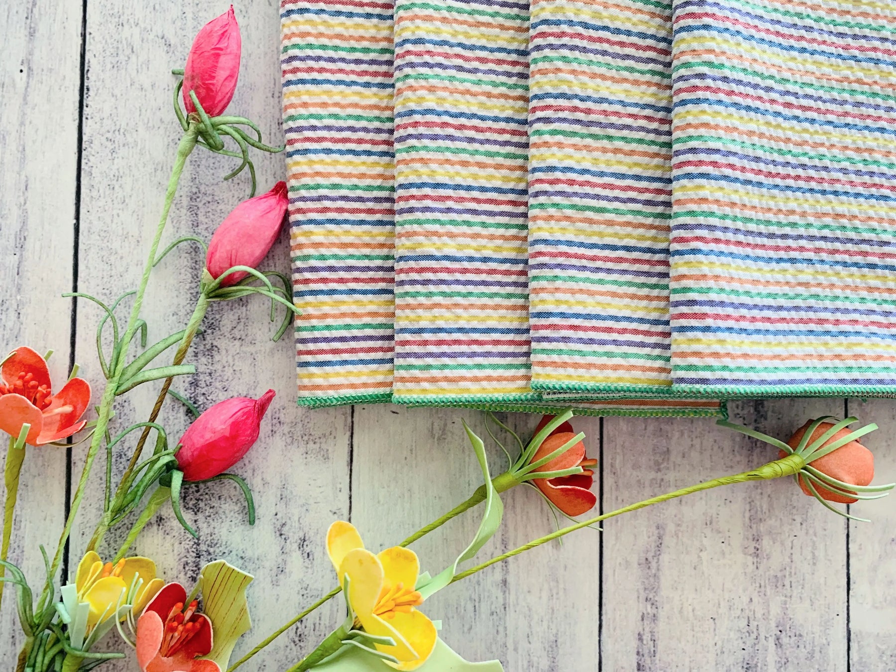 Rainbow striped seersucker cloth napkins with pink and orange paper flowers on a wooden background.