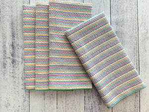 Set of four rainbow stripe seersucker cloth napkins stacked on a white wood background.