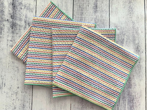 Set of four rainbow striped seersucker cloth napkins on a wood background.