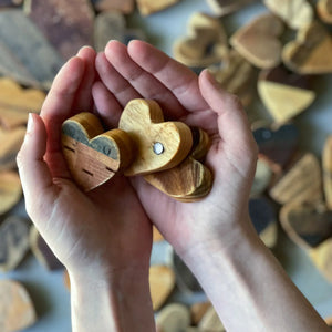 Hands holding small wooden heart shapes, with more wooden hearts in the background.