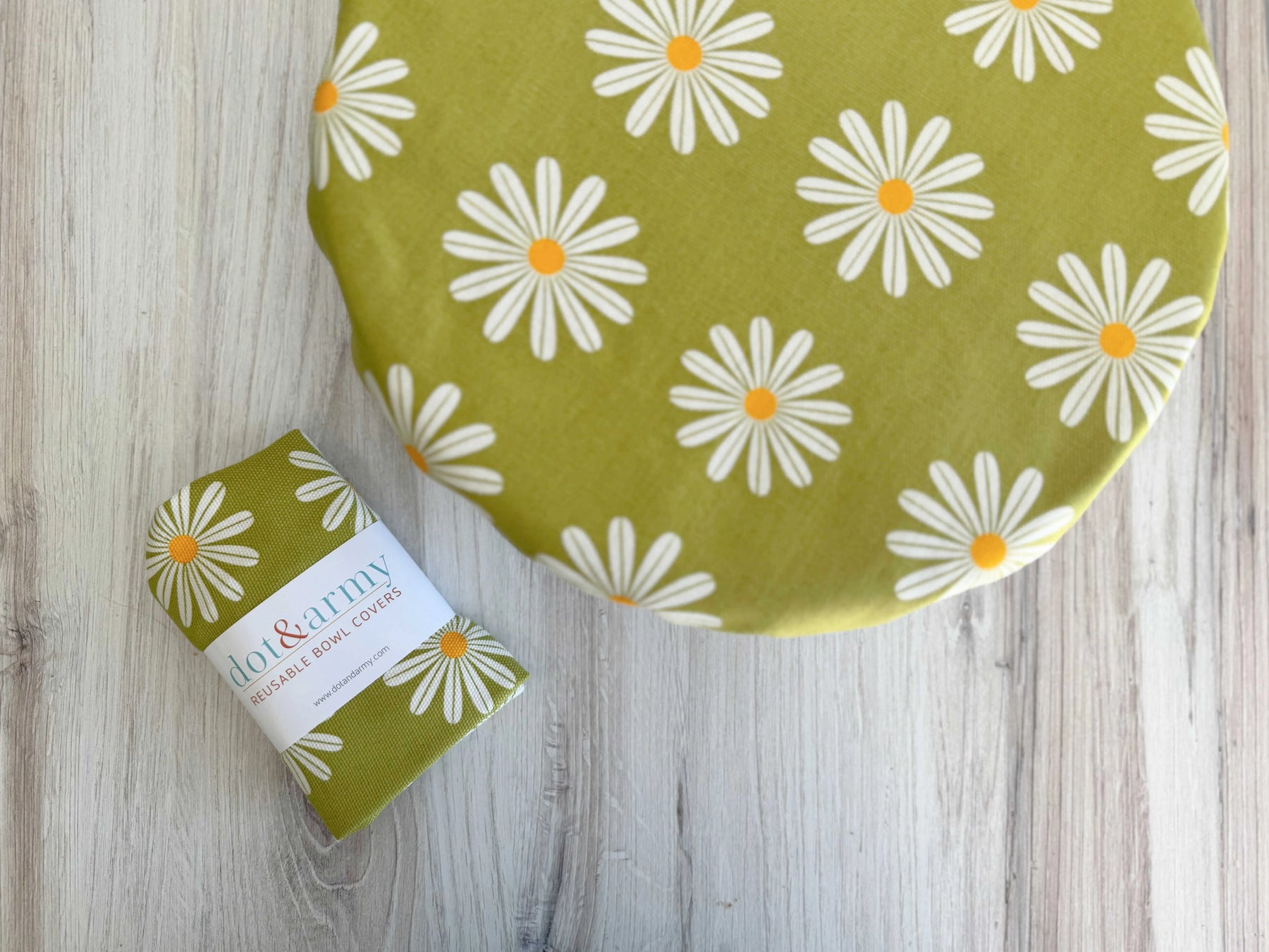 Green reusable bowl cover with white daisy pattern and white label.