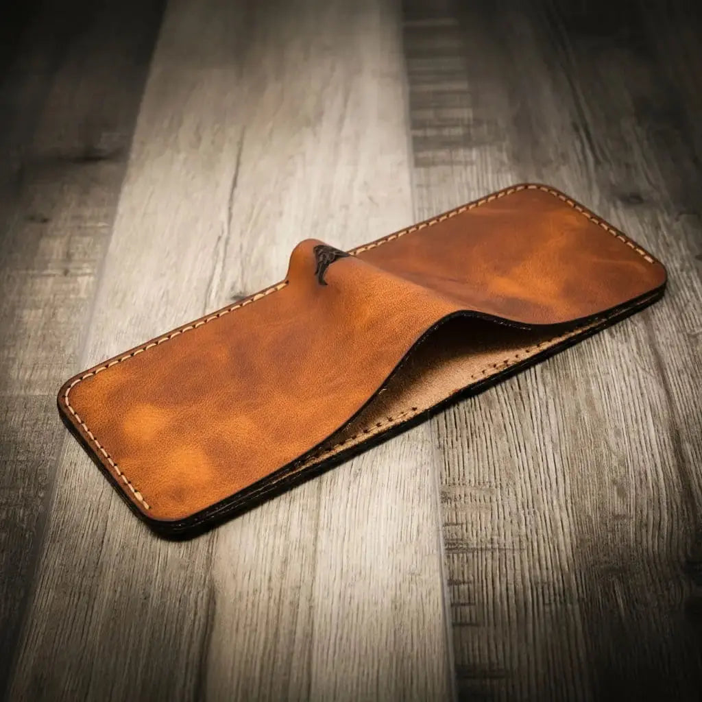 Brown full-grain leather bifold wallet with stitching on a wooden background.