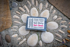 Rosemary and charcoal bar soap with wrapper on a bed of stones.
