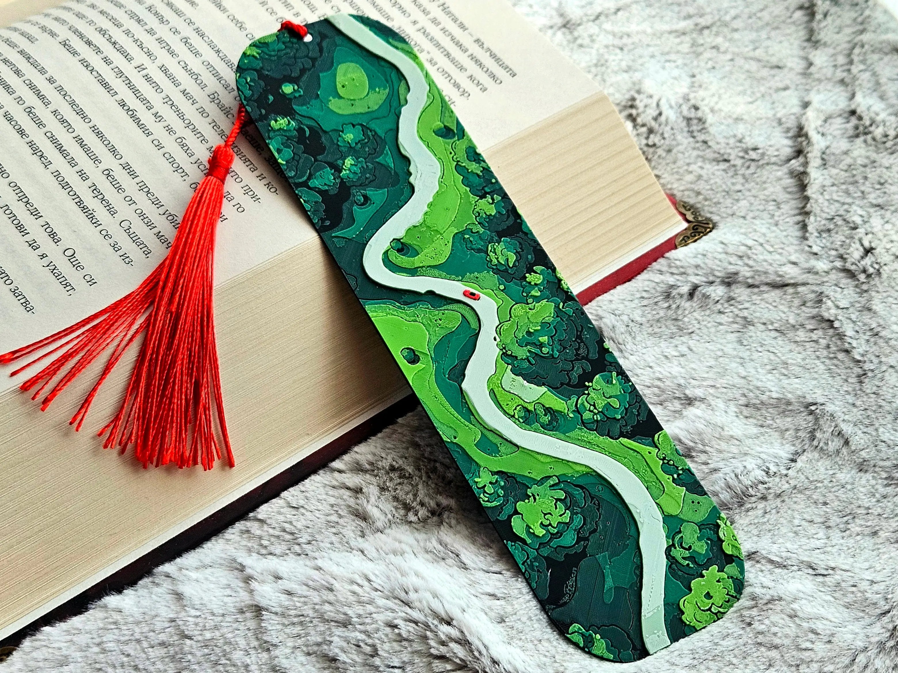 Green forest road bookmark with red tassel on an open book.