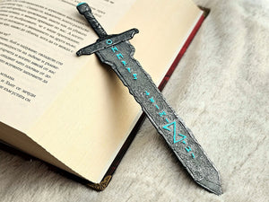 Runic blade sword bookmark with turquoise runes resting on an open book.