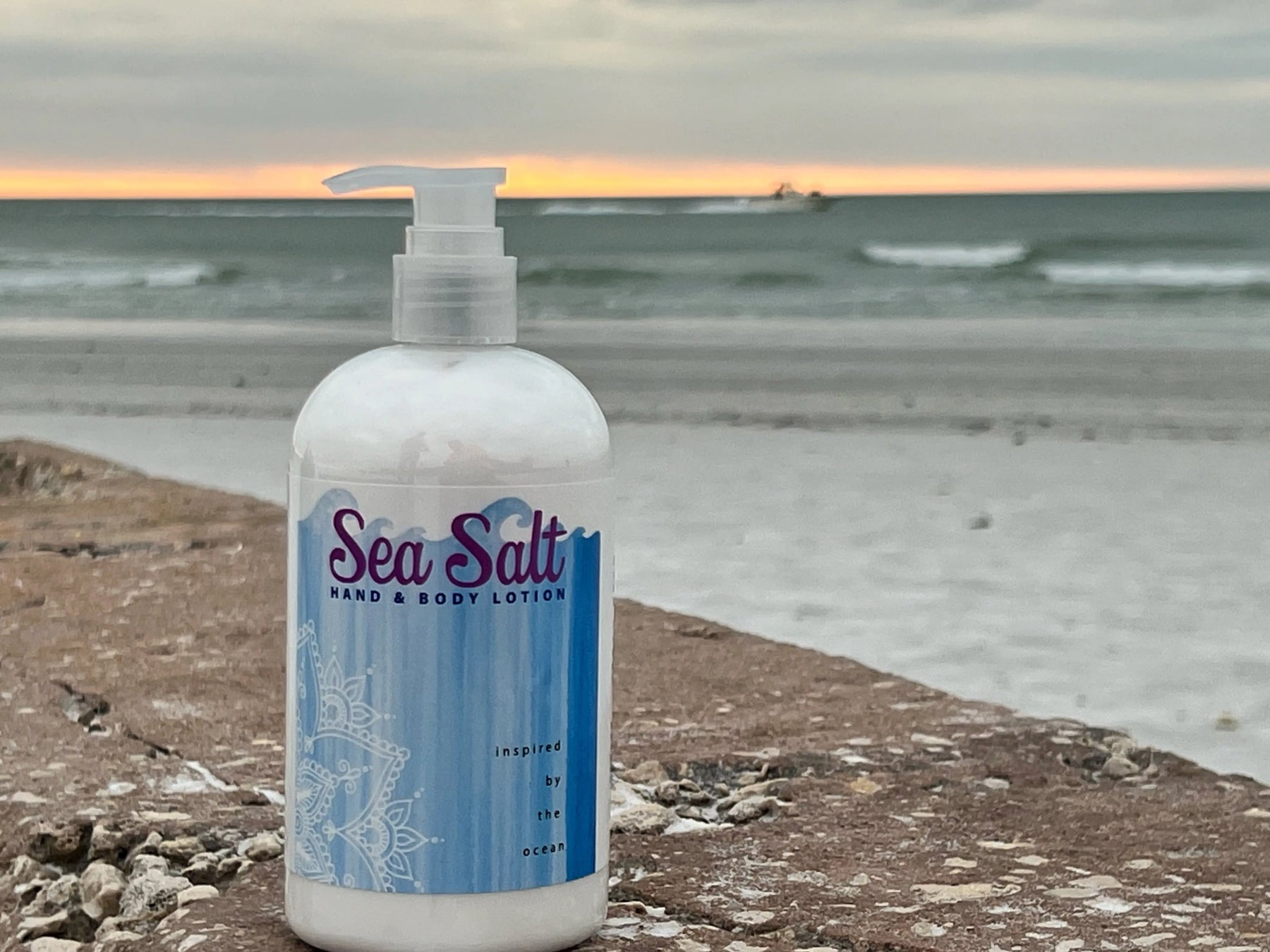 Sea Salt hand and body lotion bottle on a rocky shore with the ocean in the background.