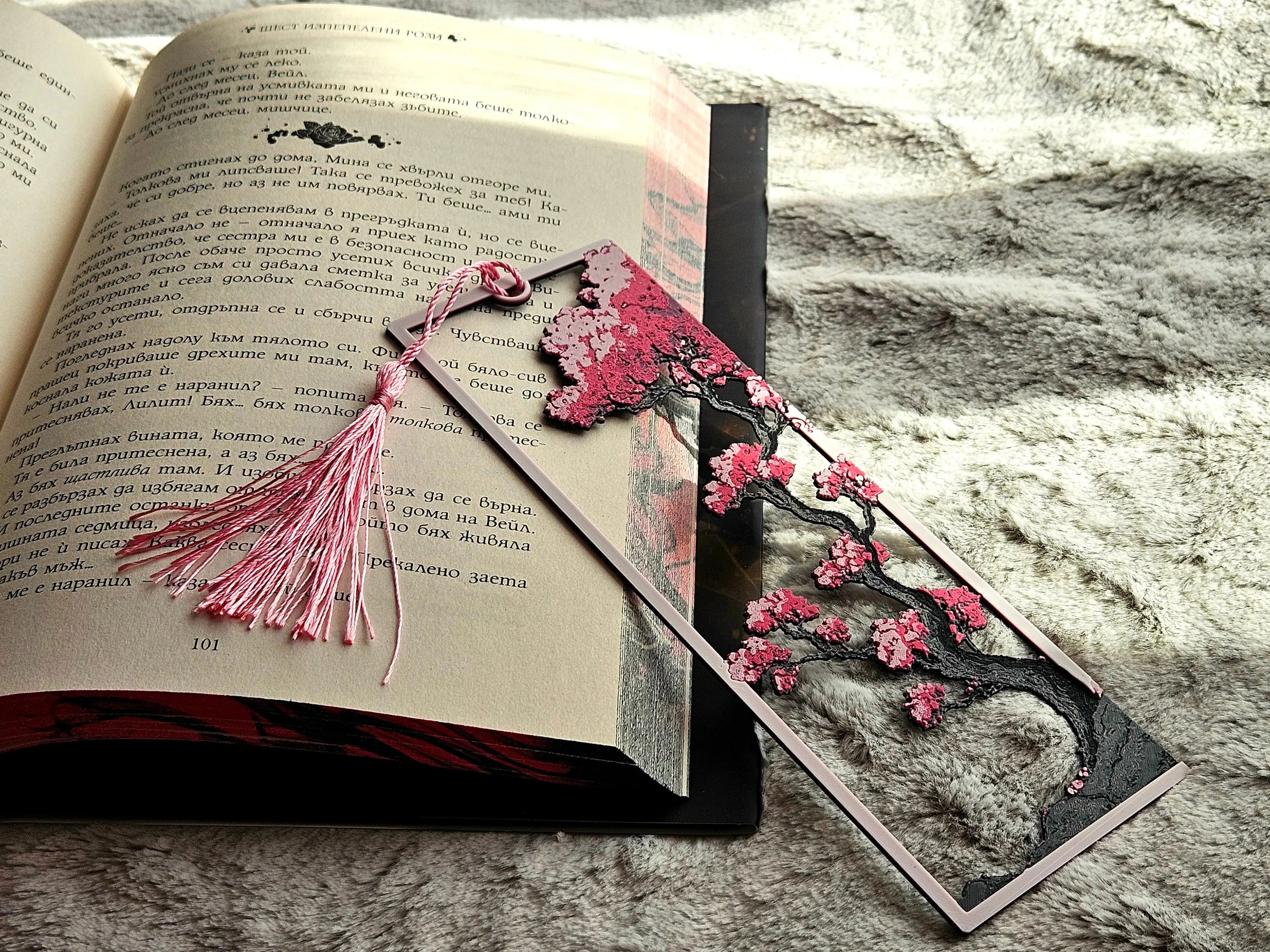 Cherry blossom bookmark with pink tassel in book. Decorative sakura tree bookmark.