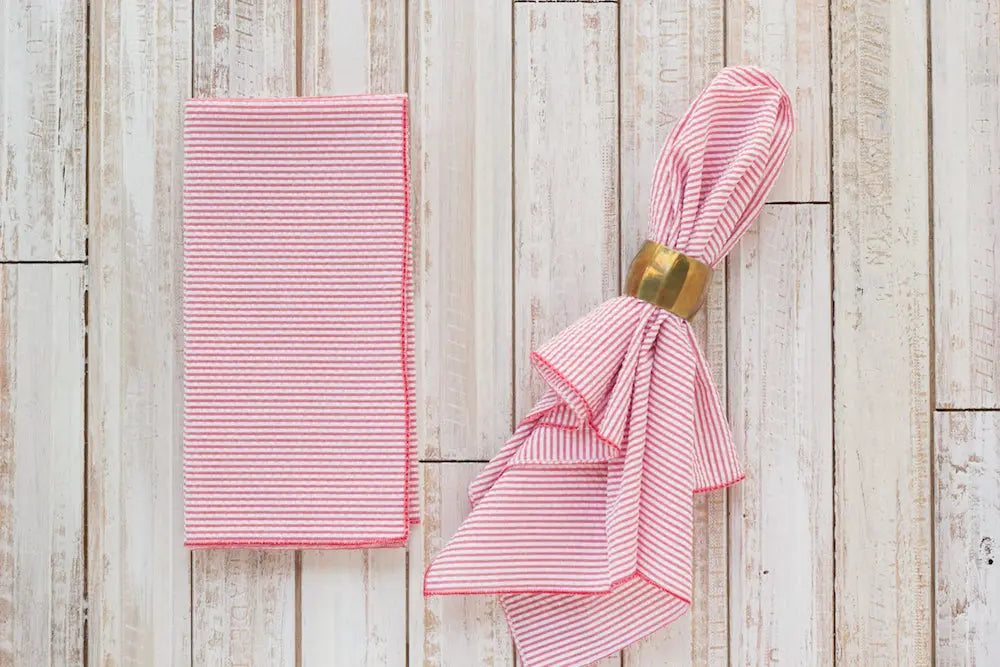 Red and white striped seersucker dinner napkin folded and with a gold napkin ring