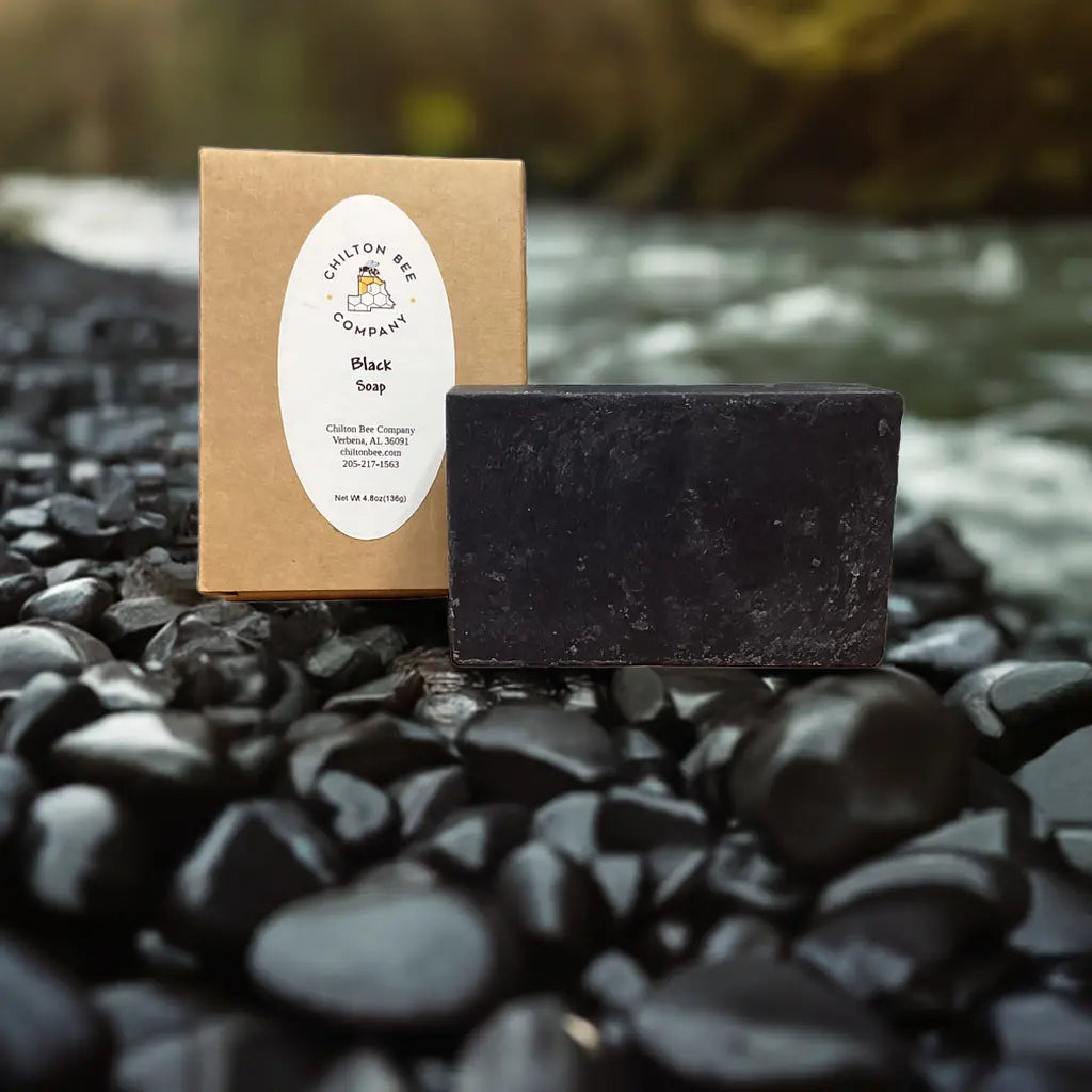 Black soap bar by Chilton Bee Company with packaging on black river rocks.