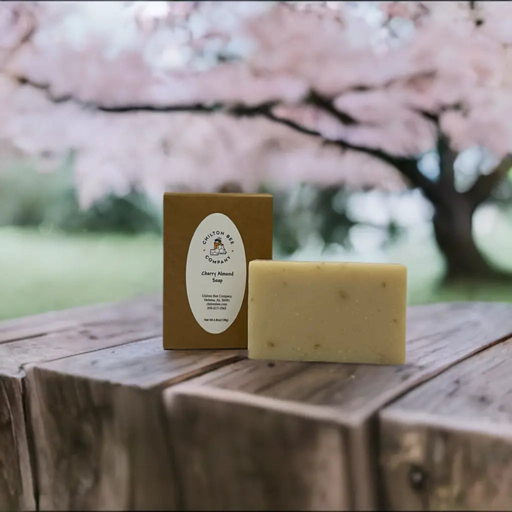 Chilton Bee Company Cherry Almond Soap bar and packaging on wood table with blurred cherry blossom tree background.