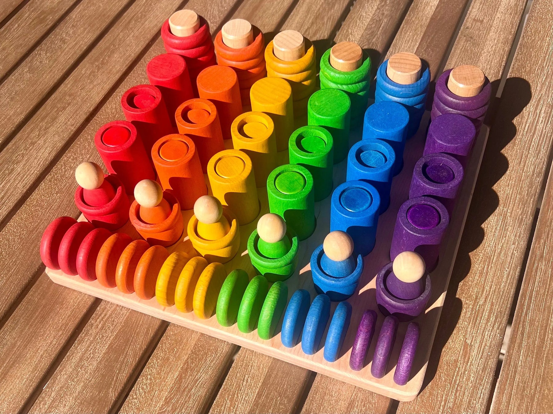 Wooden sorting tray with rainbow stacking Waldorf toys on a table.