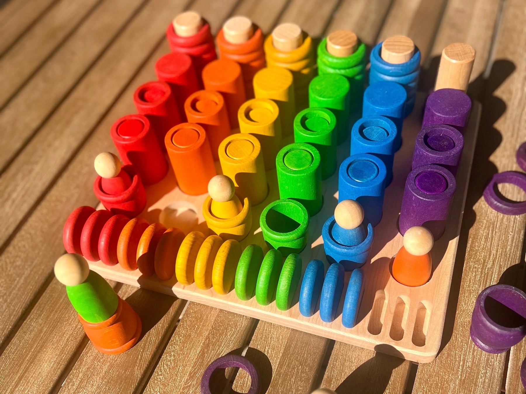 Wooden sorting tray with rainbow colored stacking pegs and cylinders.