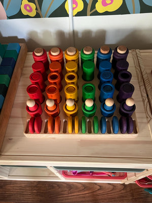Wooden sorting tray with colorful wooden peg toys arranged in rows.